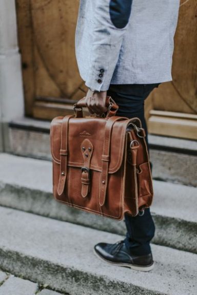ALPENLEDER Brauner Lederrucksack wird von einer Person in einem Anzug getragen.